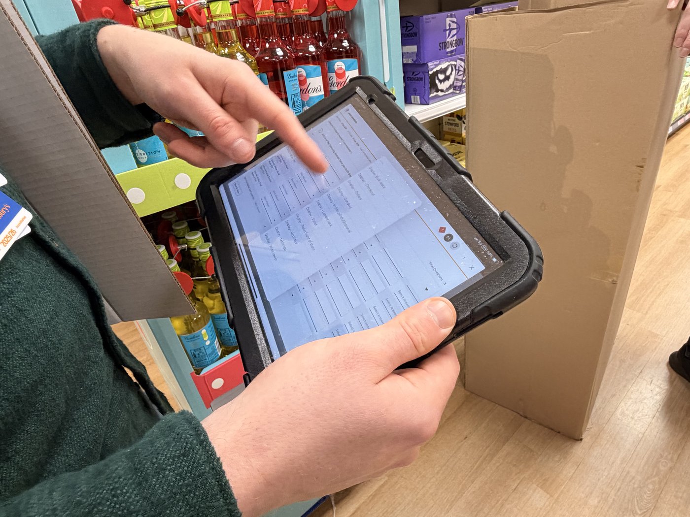 A Guinness co-packer in a store aisle filling out a compliance form on an iPad to manually prove a display had been activated